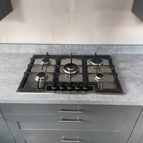 A modern gas hob with four burners, featuring stainless steel knobs and a sleek black glass surface